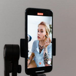 A woman records a makeup tutorial using a smartphone on a gimbal, capturing content for social media.